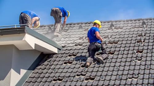 Roofers work on roof, cutting roof tiles, screwing on sunny day