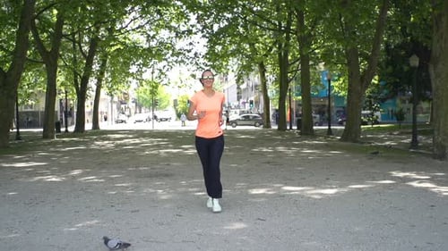 Attractive young woman jogging happily in sunny city park training for a marathon