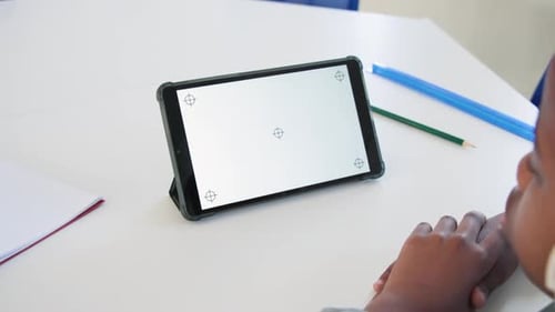 Camera panning, tablet tilting while child with headset turning and viewing screen on white desk