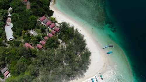 Top aerial view of a sandy beachfront with boats, cabanas, huts lining up in the forest at the ocean