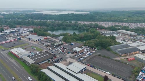 Aerial shot of an industrial zone featuring buildings, parked cars, and a water body under a cloudy