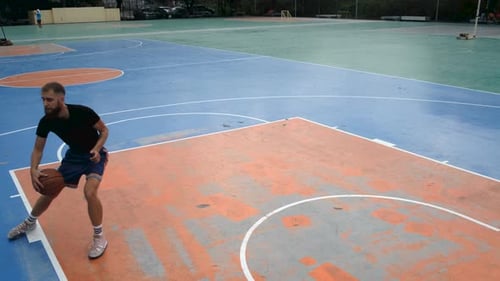 bearded man playing with a ball on a basketball court
