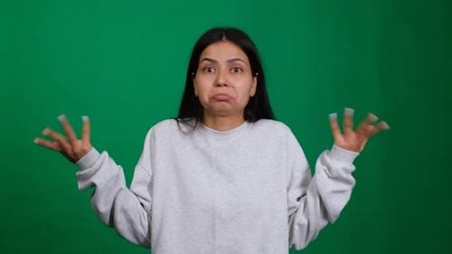 Eine junge Frau in einem Studio hebt mit einer unsicheren Geste ihre Schultern und zeigt eine verwirrte