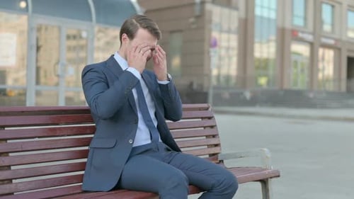 Stressed Businessman Massaging Temples on a Bench