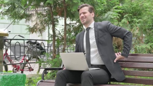 Man Sitting on Bench with Laptop Has Backache