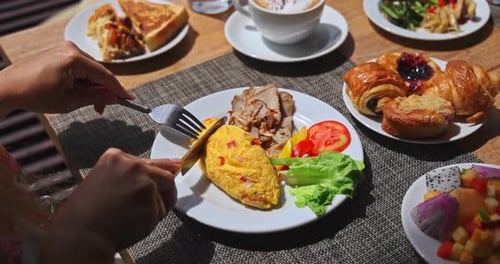 Person cutting omelet at luxury hotel breakfast buffet table