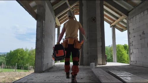 Construction Worker Carrying Tools Walks Through Building