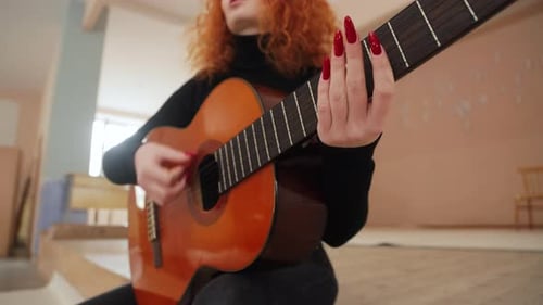 Close-up video of a woman playing chords on an acoustic guitar while sitting on stage in a room.