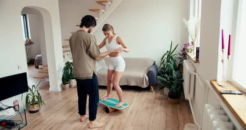 The Guy Helps the Girl Stand on an Unstable Structure to Improve the Vestibular Apparatus and