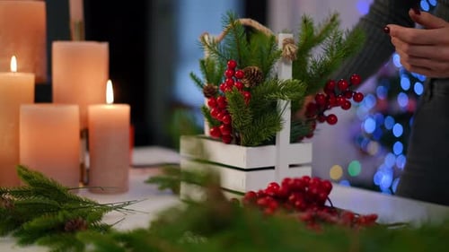 Unrecognizable Young Woman Making Handmade Christmas Decoration in Decorative Basket Mixing Green