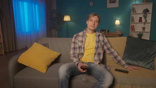 A Man is Resting After a Hard Day's Work Sitting in the Evening on the Sofa in Front of the TV with