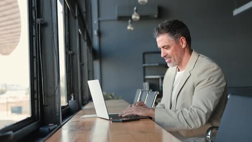 Happy Mid Aged Business Man Sitting in Modern Office Working on Laptop