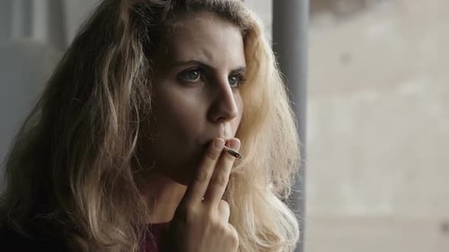 serious beautiful woman smokes a cigarette looking away lost in her thoughts