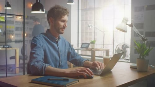 Handsome Creative Male in Jeans Shirt Works on a Laptop in His Sunny Loft Office. He Looks Cool and