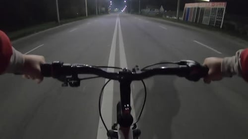 A Man Riding Bicycle Along Center of Highway Night Under Light of Lanterns
