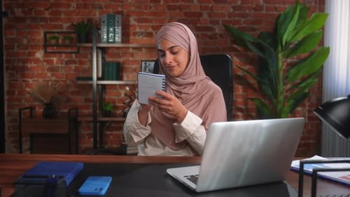 Femme contemplative en hijab tenant un carnet au bureau