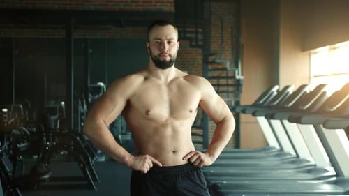Medium Shot of Muscular Man with Bare Torso and Hands on Waist Posing in Gym