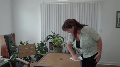 Middle aged caucasian woman wiping a dining room table.