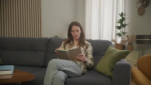 Woman Reads Book on Sofa Indoors