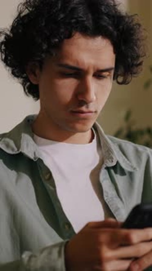 Young Man Looks at Phone Indoors During Daytime