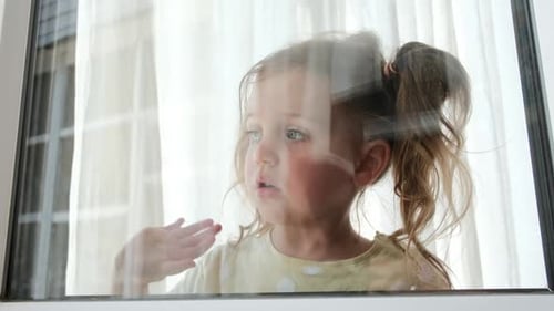 Pretty Little Girl Waves Hand Looking Out of Window at Home