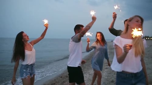Amigos caminhando, dançando e se divertindo durante a festa noturna à beira-mar com luzes cintilantes de Bengala