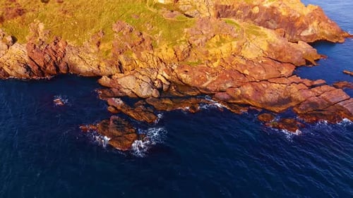 Rocks and ocean meet at the edge of a rugged coastline during sunset.