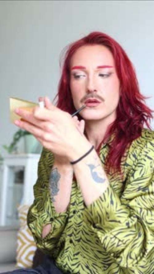 vertical Redhead non-binary person applying lipstick in front of a mirror