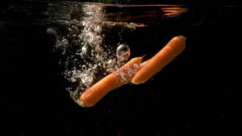 Three juicy carrots drowning slowly together in the dark and clear water. Steady underwater slow mot