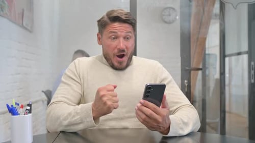 Excited Man Using Smartphone in Office Setting