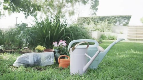Close up of watering cans, flowers and pots in sunny garden, slow motion