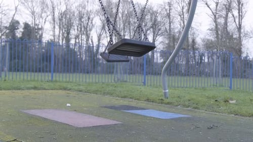 Empty swinging swing on children playground with no people on a cloudy cold day in central London. S