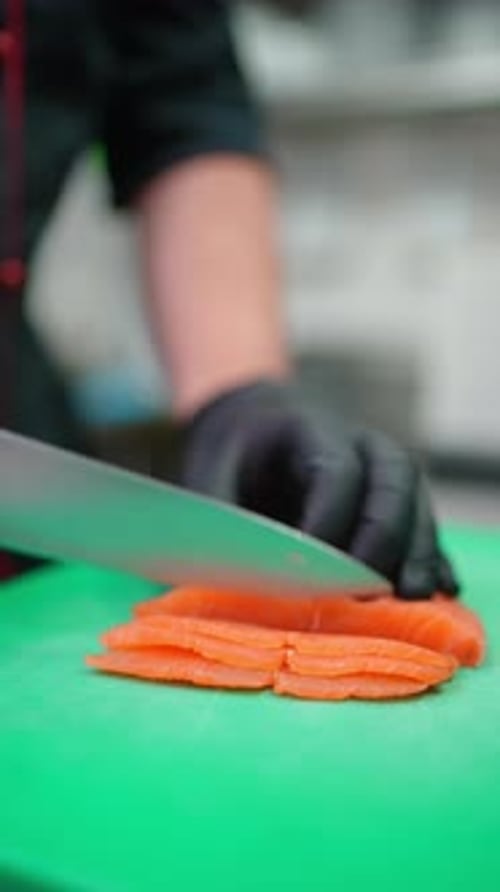 Professional Chef in Black Gloves Carefully Slicing Fresh Salmon Fillet Into Thin Sashimi Pieces on
