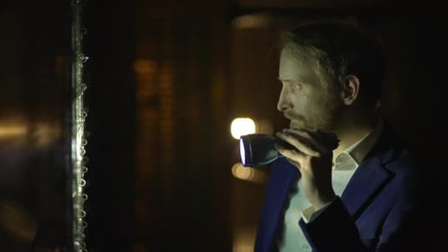 Man in Suit Spies at Night Investigating Bank Vault Safe Holding a Flashlight in Dark Room