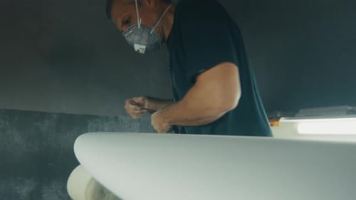 Surf factory. Adult male shaper creates the surfing board on the factory