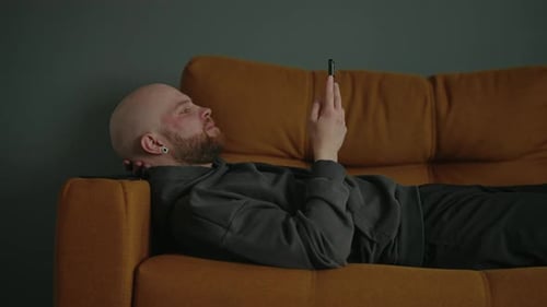 Man Lies on Couch Using Cell Phone
