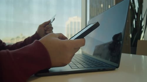 Vista lateral do jovem usando laptop e smartphone para compras on-line no café