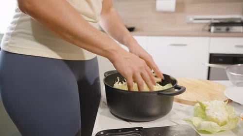 Woman Putting Freshly Cut Cabbage into Black Pot in Kitchen with Side View, Concept Healthy Eating