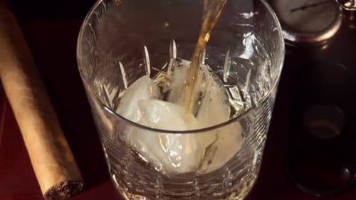 Whiskey Being Poured Over Ice Next to Cigar