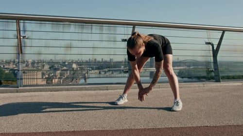 Fitness young sportswoman girl in the morning doing warm-up exercises before training on the street