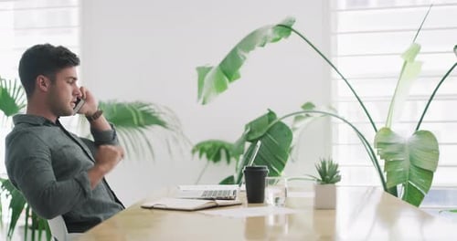 4k video footage of a young businessman talking on a cellphone and using a laptop in an office