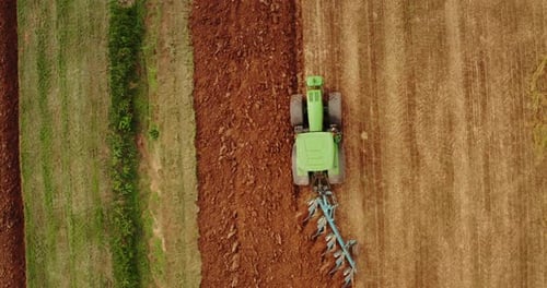 Aerial shot of farming tractor is collecting a straw on a field for making hay bales in a sunny da