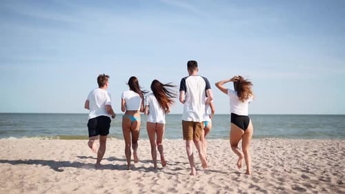 Group of Happy Friends Undress Running Into the Sea Water and Throw Shirts on the Beach Cheerful