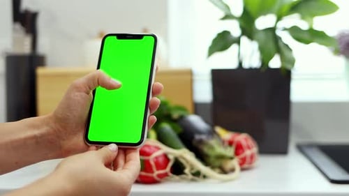 Close-up of female hands holding smartphone with green screen on a background of organic vegetables