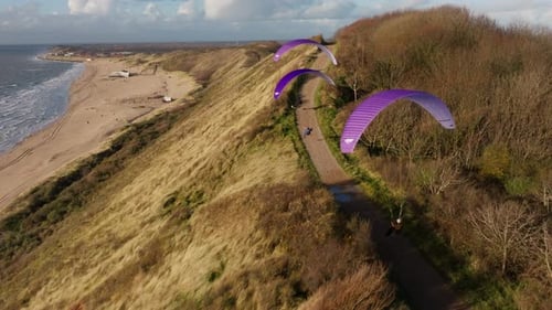Aerial view of paragliders flying along cliffs and sandy coastline under a bright sky
