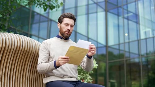 Man Reading Letter Looking Frustrated Outdoors