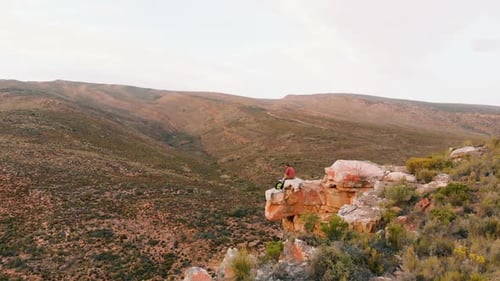 Young Caucasian man sits on a cliff edge, outdoor with copy space