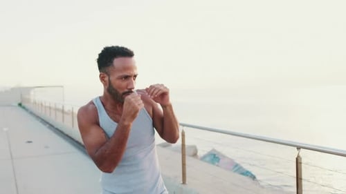 Young fit athlete boxer practicing punching technique while standing on the embankment