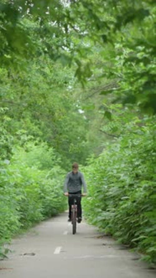 Young Boy Riding Bicycle Through Scenic Green Tunnel on Paved Pathway