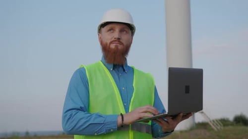 An Engineer Working on a Laptop at a Wind Farm Focused on Sustainable Energy Solutions